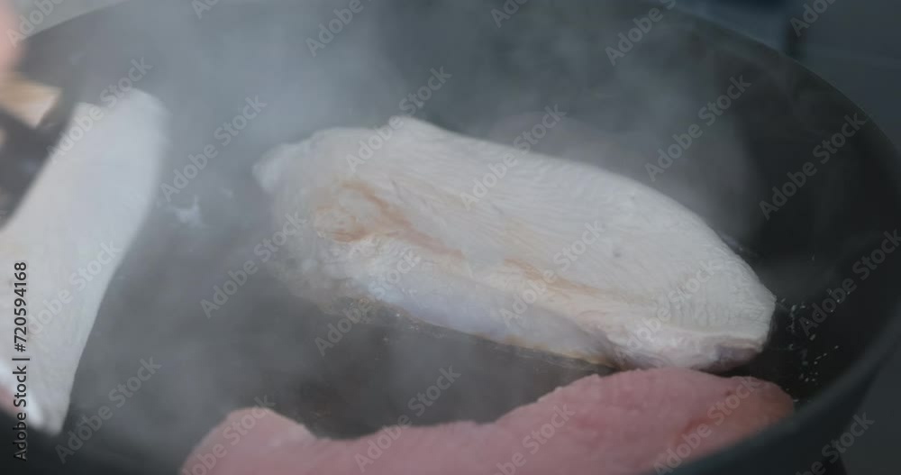 A woman flipping over a turkey breast in a frying pan using a spatula. Close up. A woman flipping over a turkey breast in a frying pan using a spatula. Close up.