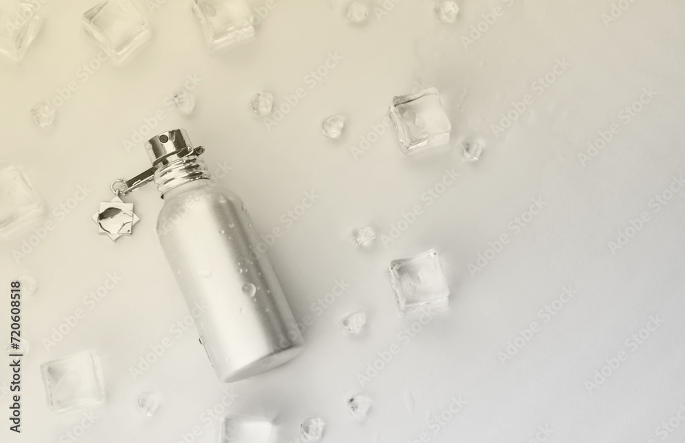 Naklejka premium Female perfume silvery bottle, Objective photograph of metallic perfume bottle in ice cubes and water on white table. View from above. Mockup product photo, concept of freshness and aroma