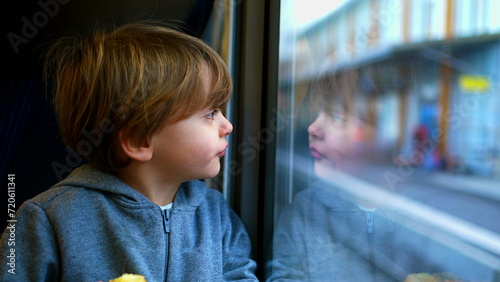 One small boy traveling by train leaning on glass staring at view, reflection of child's face on window