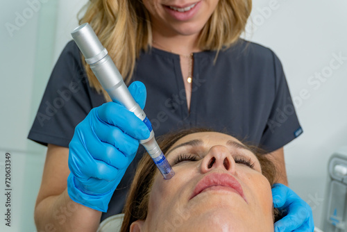 close-up young female esthetician with microneedling pen on old woman photo