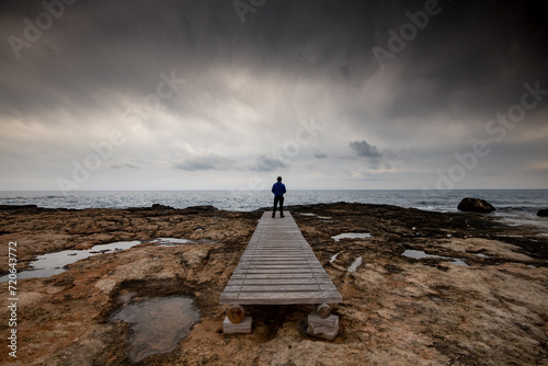 Man standing alone at the edge of rocky beach in Stormy Weather. Cape Greko Cyprus. photo