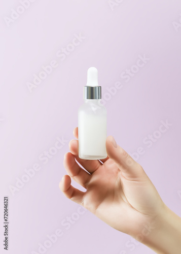 hand holding white serum in a glass bottle on a pink background. skin care concept