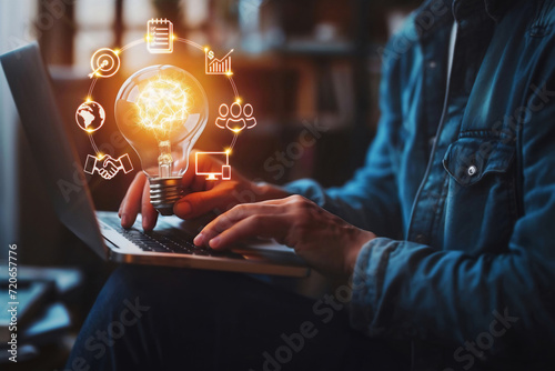 Businessman Hand holding Light bulb with a laptop. Glowing icons of global, internet, connection, technology, digital, marketing, financial, banking, innovation, application,  data etc are around bulb photo