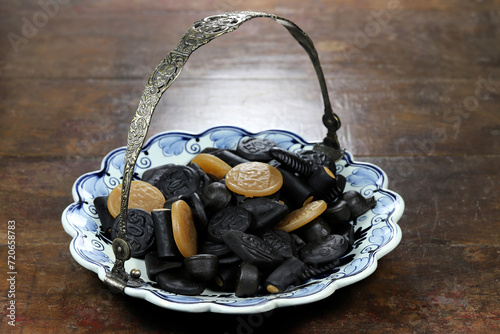 Dutch licorice candies on a Delftware plate on wooden background photo