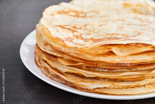 A round dish with fried pancakes on a brown table. A sweet dessert for breakfast. Sunny morning.