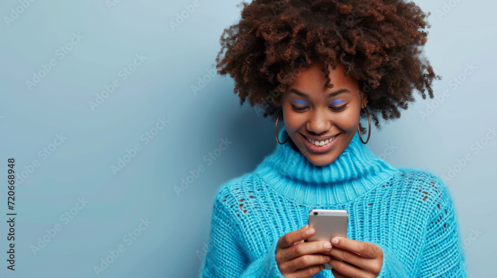 young woman with a vibrant afro hairstyle is smiling and looking at her smartphone, wearing a cozy turquoise turtleneck sweater against a matching turquoise background young woman with a vibrant afro hairstyle is smiling and looking at her smartphone, wearing a cozy turquoise turtleneck sweater against a matching turquoise background