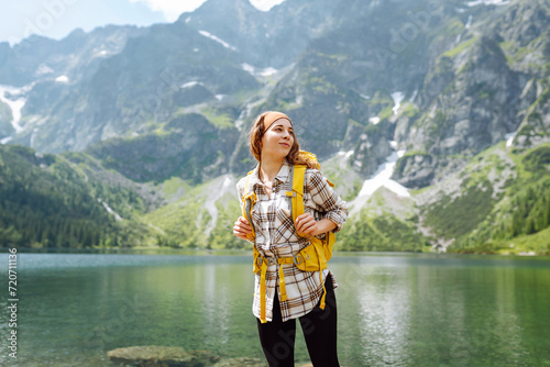 Young woman with backpack near lake on wooded mountains background. Amazing landscape. Enjoying nature. Concept of weekends trip. Active lifestyle.