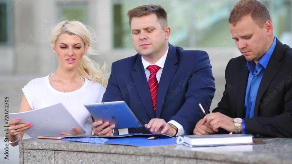Three office workers standing on the street with papers and a tablet