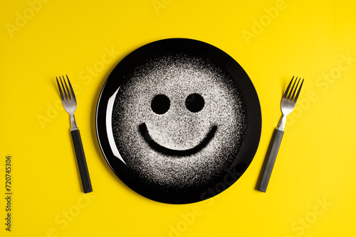Smiling face, concept made with plate and flour, yellow background, star shaped eyes, black plate, happy mood, facial expressions, forks in the shape of arms with different positions