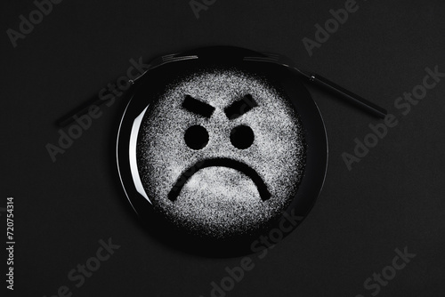 Displeased face, frowning eyebrows, concept made with plate and flour, black background, black plate, facial expressions, forks in the shape of arms with different positions
