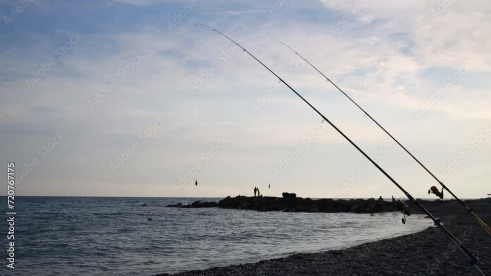 Two fishing rods standing on the shore of the sea at sunset Two fishing rods standing on the shore of the sea at sunset