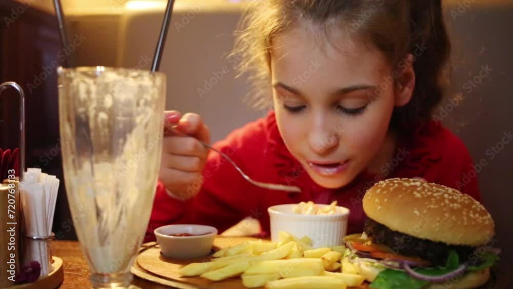 Girl eats salad, french fries and hamburger are on table in restaurant Girl eats salad, french fries and hamburger are on table in restaurant