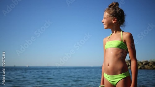Girl in a green bathing suit standing by the sea on a sunny day