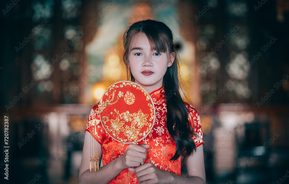 Portrait beautiful Asian young woman wearing red traditional Chinese cheongsam decoration and holding a Chinese Fanning in Chinese New Year Festival at Chinese shrine in Thailand