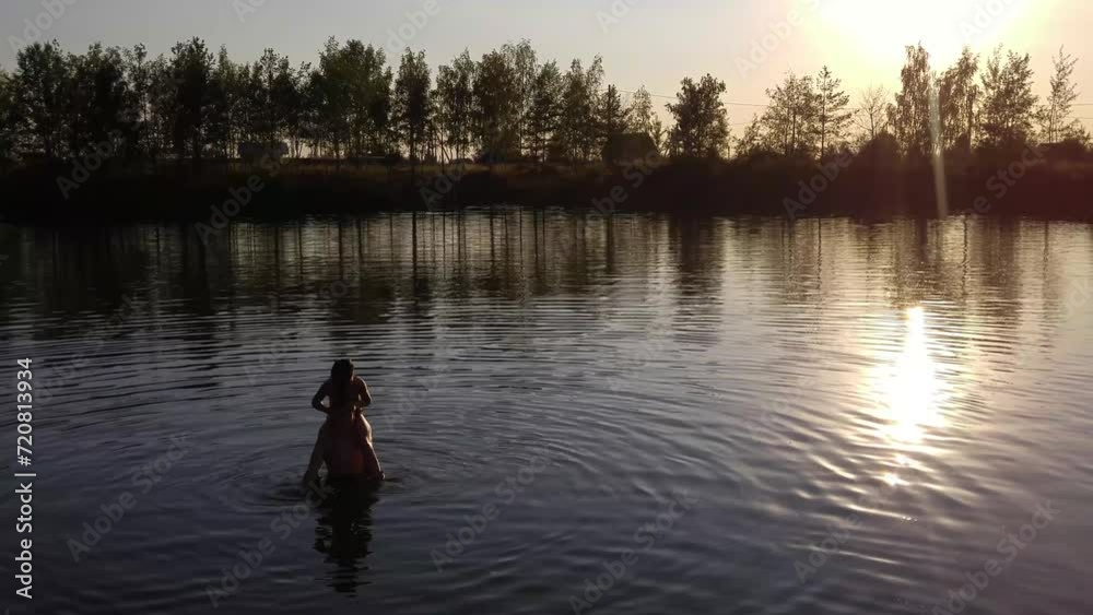 Girl sitting on boys shoulders in water of lake at sunset, mobile phone video. Girl sitting on boys shoulders in water of lake at sunset, mobile phone video.