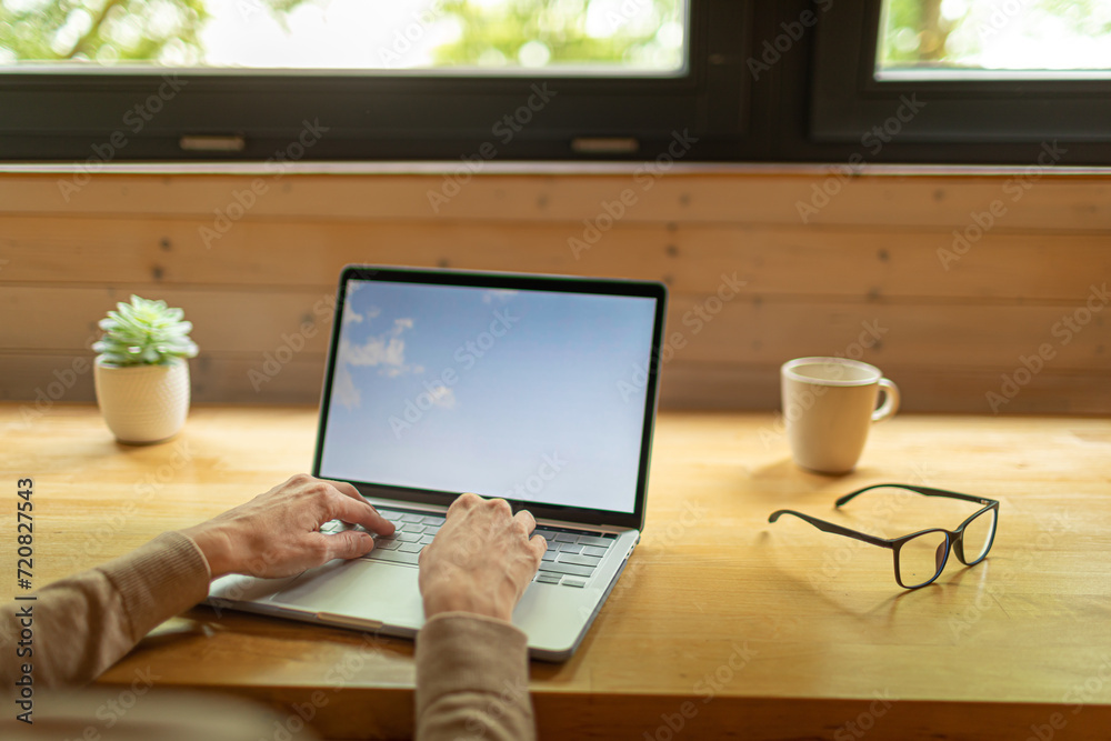 Fototapeta premium person working on laptop on office desk next to window