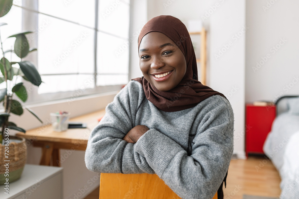 Portrait of young african girl smiling at camera while relaxing on her room. Proud people and religion concept.