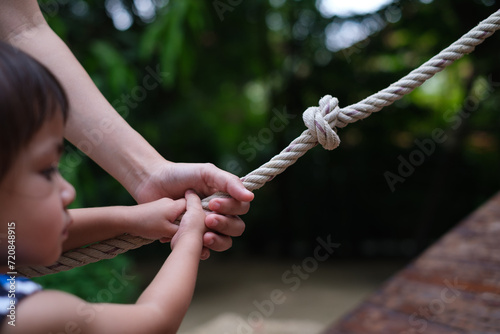 Parent and child holding hand together while climbing rope. love and care family. Life growth for the future plan. Parent support the kid Guidance in the right way