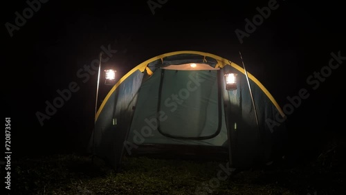 An tent glowing in the darkness with a tourist inside photo