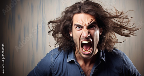 Angry young man screaming and pulling his hair in front of a wall