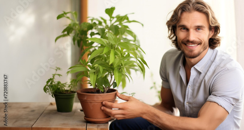 Handsome young man holding a pot with a plant at home