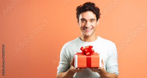 Portrait of a happy young man holding gift box on orange background