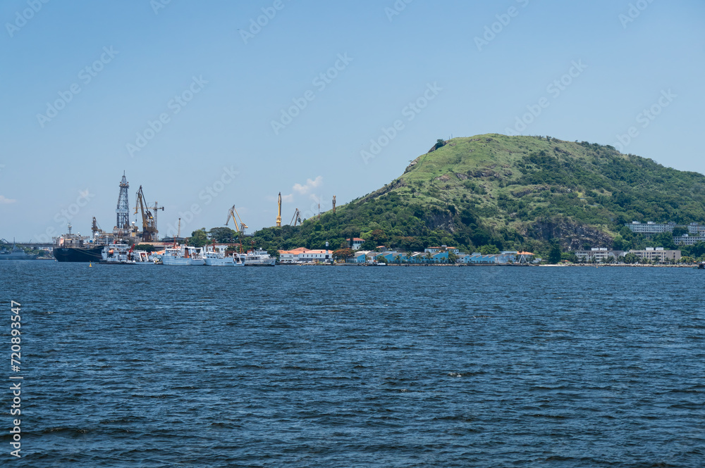 Partial view of Morro da Penha hill in Niteroi's Ponta Dareia district as saw from Guanabara bay blue waters under summer afternoon sunny clear blue sky.