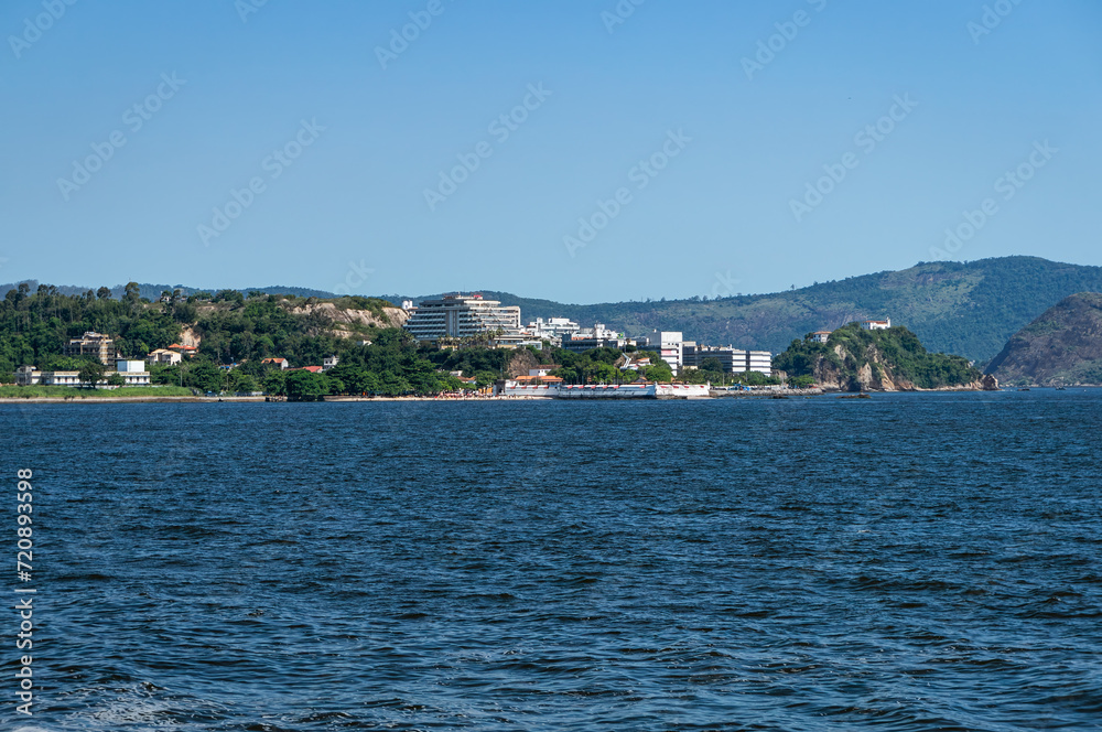 Distant view of Niteroi's Sao Domingos and Gragoata districts coastline as saw from Guanabara bay blue waters under summer afternoon sunny clear blue sky.