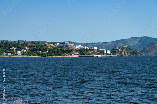Distant view of Niteroi's Sao Domingos and Gragoata districts coastline as saw from Guanabara bay blue waters under summer afternoon sunny clear blue sky.