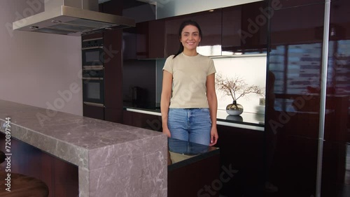 Dark-haired woman stands in kitchen with her arms crossed, woman folds her arms hesitantly, light-skinned woman in the kitchen looks into the frame with her arms crossed and thinks about what to cook.