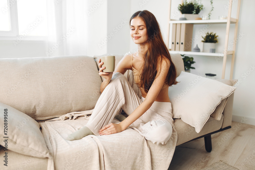Cozy Autumn Morning: Smiling Woman Drinking Coffee, Wrapped in Blanket, Relaxing on Sofa at Home