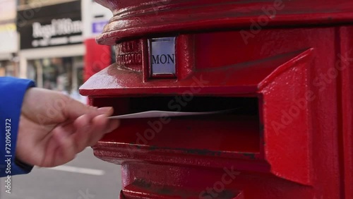 Sending a postcard. Close-up of a man's hand sending a postcard into a red postbox in London photo