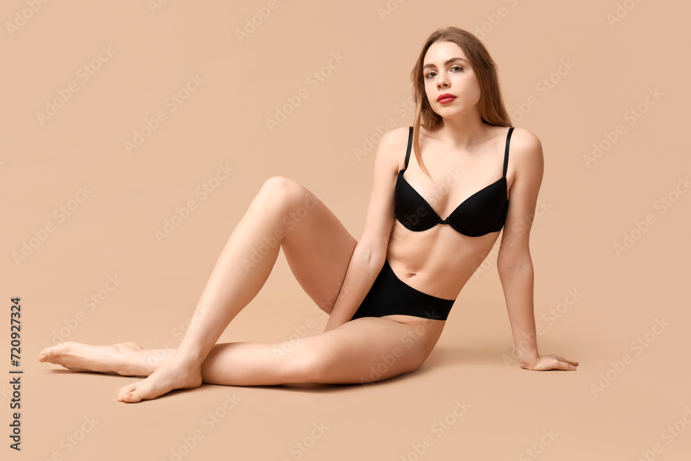 Beautiful young woman in black underwear sitting against beige background