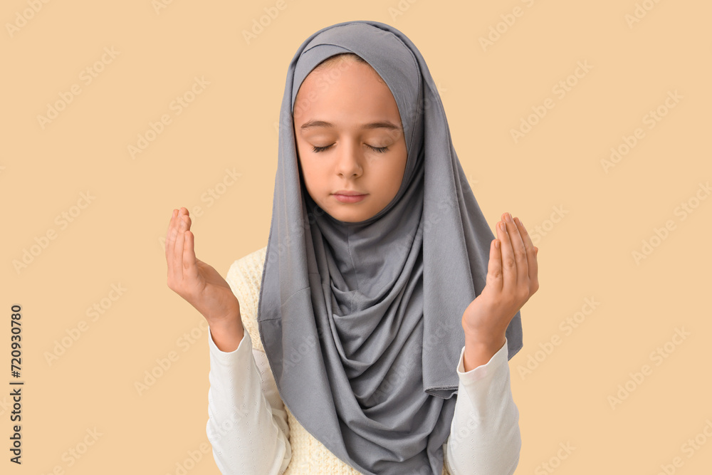 Little Muslim girl in hijab praying on beige background Little Muslim girl in hijab praying on beige background