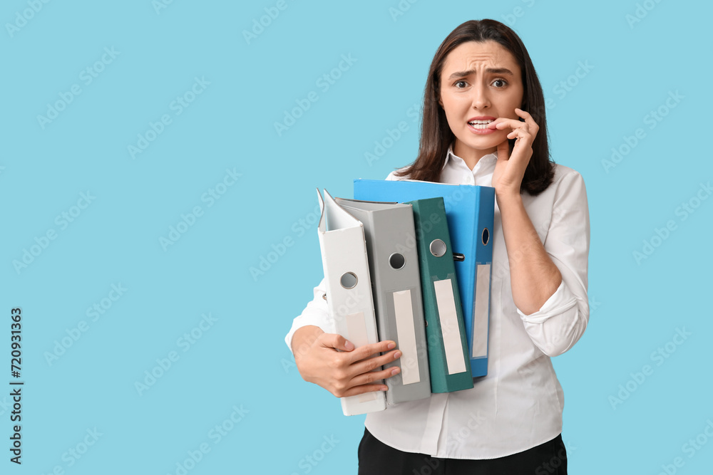 Stressed young businesswoman with document folders on blue background Stressed young businesswoman with document folders on blue background