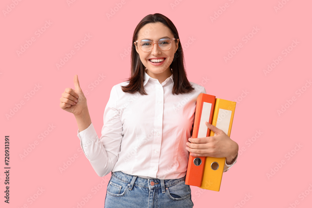 Young businesswoman with document folders showing thumb-up on pink background Young businesswoman with document folders showing thumb-up on pink background