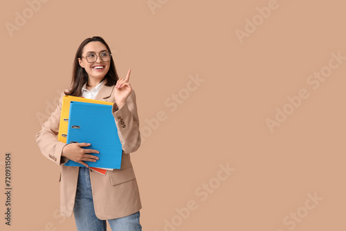 Young businesswoman with document folders pointing at something on beige background © Pixel-Shot