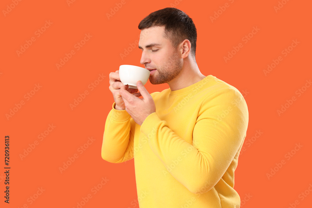 Young man drinking tea on orange background Young man drinking tea on orange background