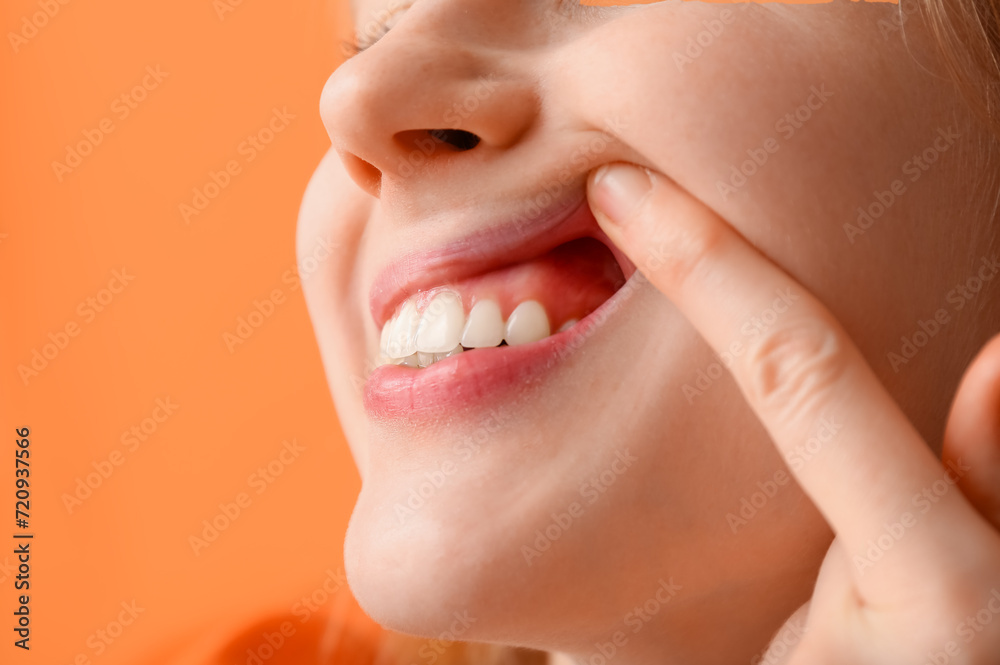 Obraz premium Teenage girl showing her teeth on orange background, closeup