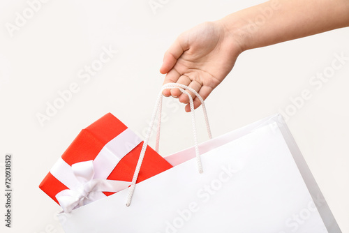 Female hand with paper shopping bag and gift box on white background. Valentine's Day celebration © Pixel-Shot