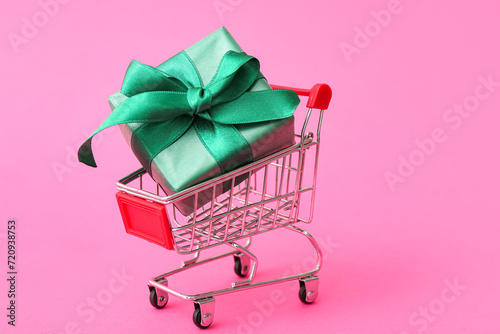 Small shopping cart with gift box on pink background. Valentine's Day celebration