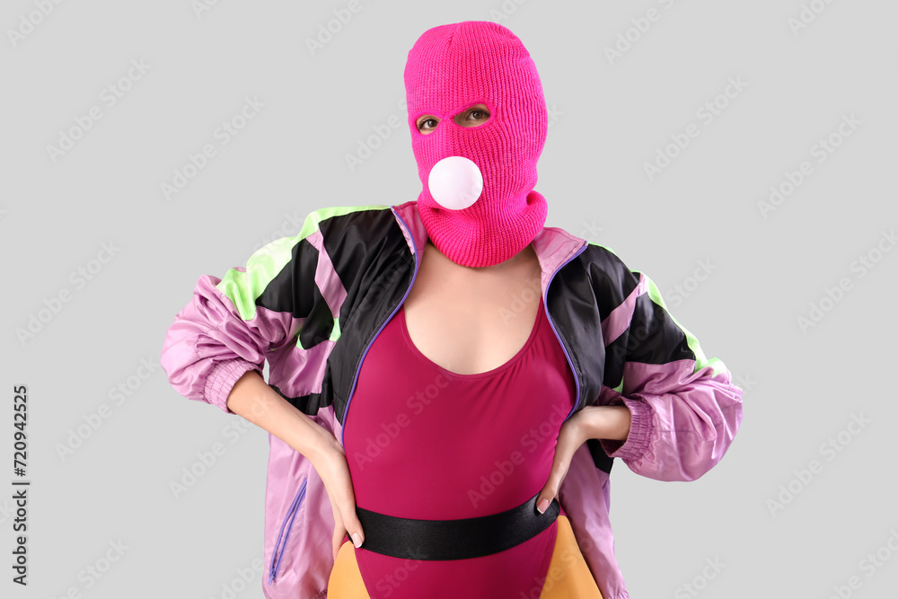 Beautiful young stylish woman in balaclava with gum on grey background Beautiful young stylish woman in balaclava with gum on grey background