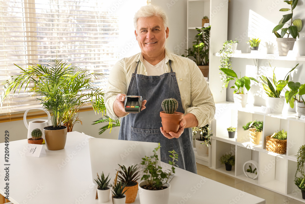 Mature man with cactus and payment terminal in flower shop Mature man with cactus and payment terminal in flower shop