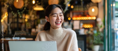 Asian woman happy with laptop, achieving work goal, smiling in cafe.