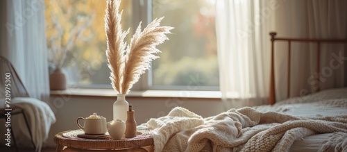 Cozy fall morning in a country house with a relaxing atmosphere and a bed covered in a blanket, featuring beautiful boho interior details like pampas grass in a vase on a coffee table to set a hygge