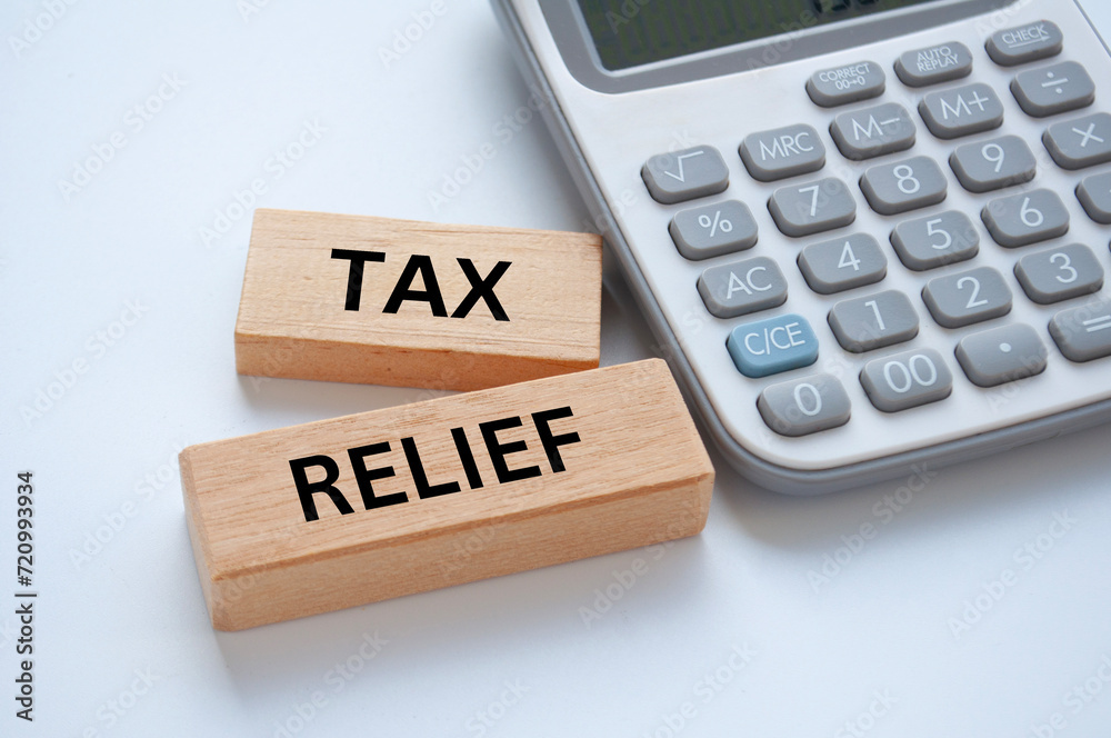 Tax relief text on wooden blocks on white cover background with calculator background. Taxation concept Tax relief text on wooden blocks on white cover background with calculator background. Taxation concept