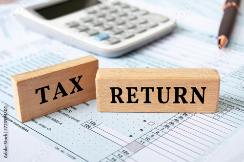 Tax return text on wooden blocks with tax form and calculator background. Taxation concept photo