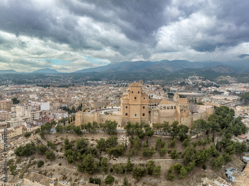Aerial view of Caravaca de la Cruz castle dominating the landscape with square and circular towers, medieval palace and Baroque ornament facade church