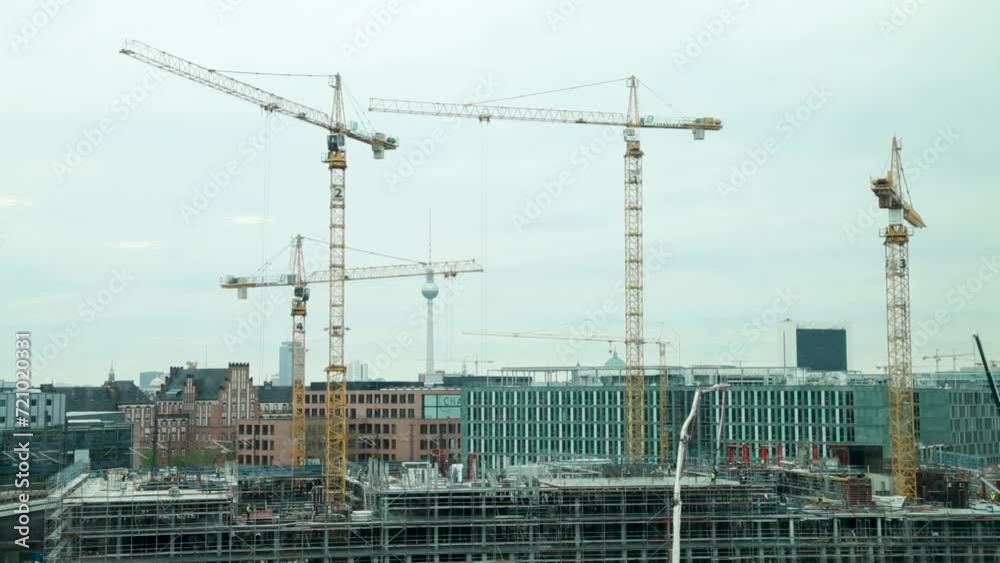 Construction cranes towering over a building site in Berlin with the iconic TV Tower in the background Construction cranes towering over a building site in Berlin with the iconic TV Tower in the background