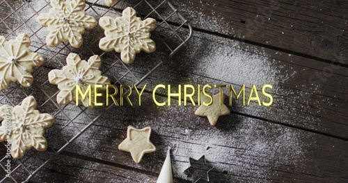 Merry christmas text in yellow over snowflake cookies on wooden background